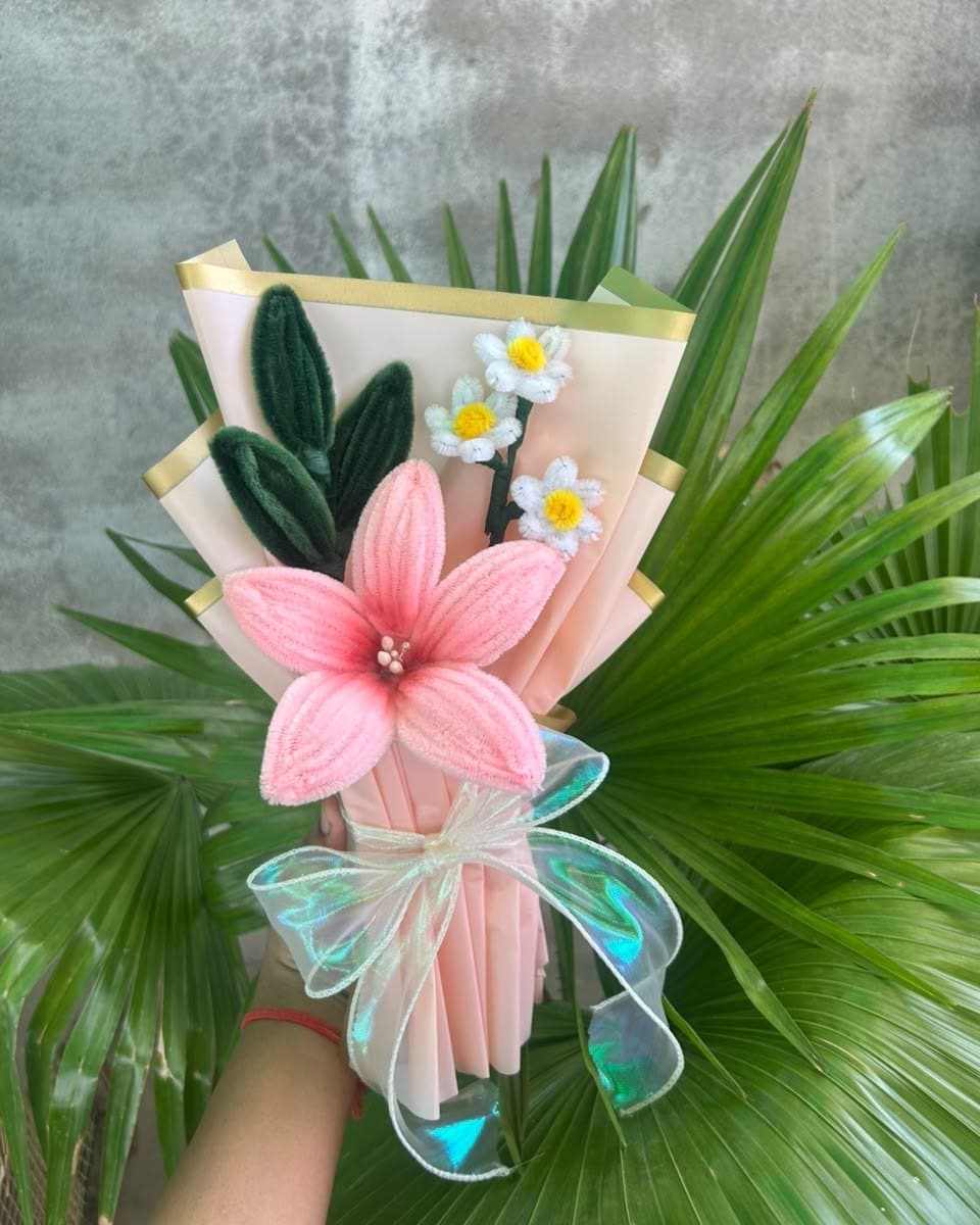 Pink pipe cleaner lily and daisy bouquet in front of green palm leaves