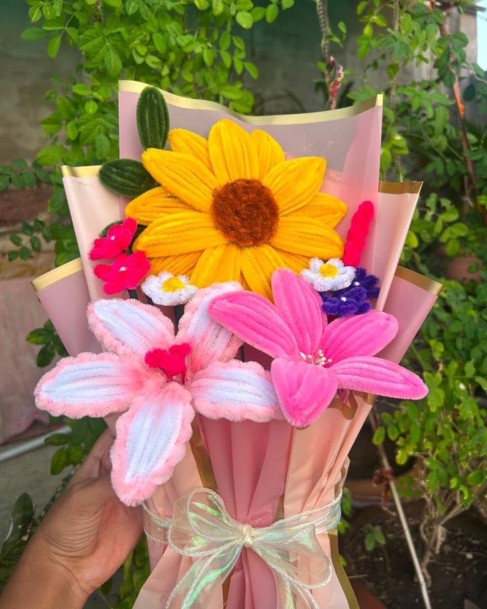Close view of a pipe cleaner sunflower and two lilies in blush wrapping paper