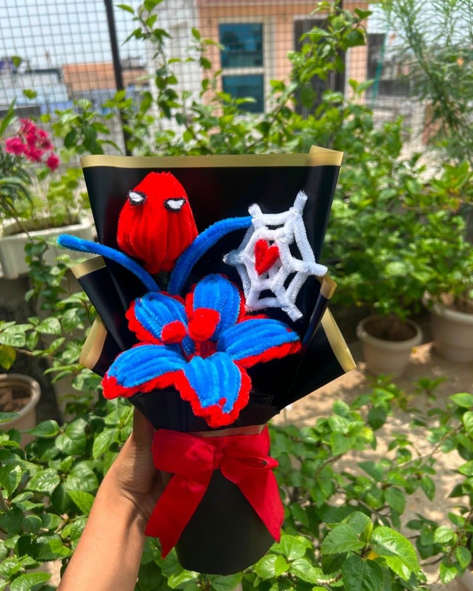Red and blue pipe cleaner bouquet with a tulip, a lily and a white web holding a red heart, in black paper