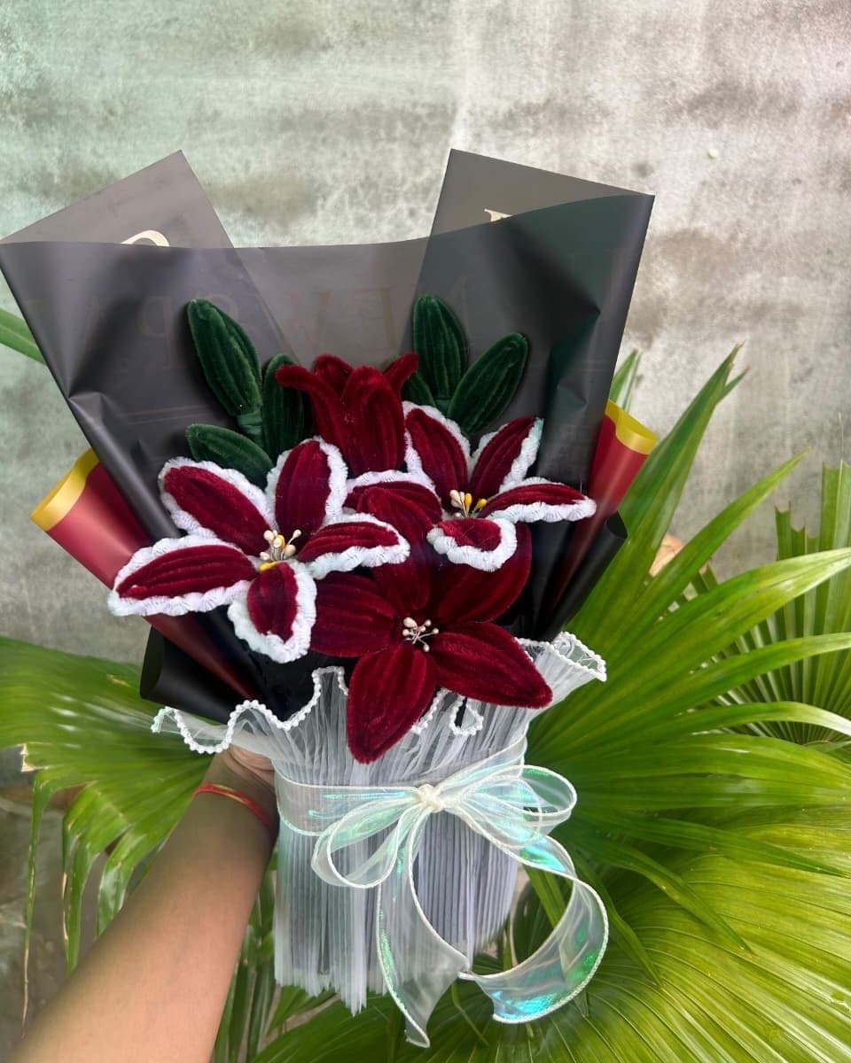Pipe cleaner bouquet of four maroon lilies edged in white, wrapped in black paper with a white pleated wrap
