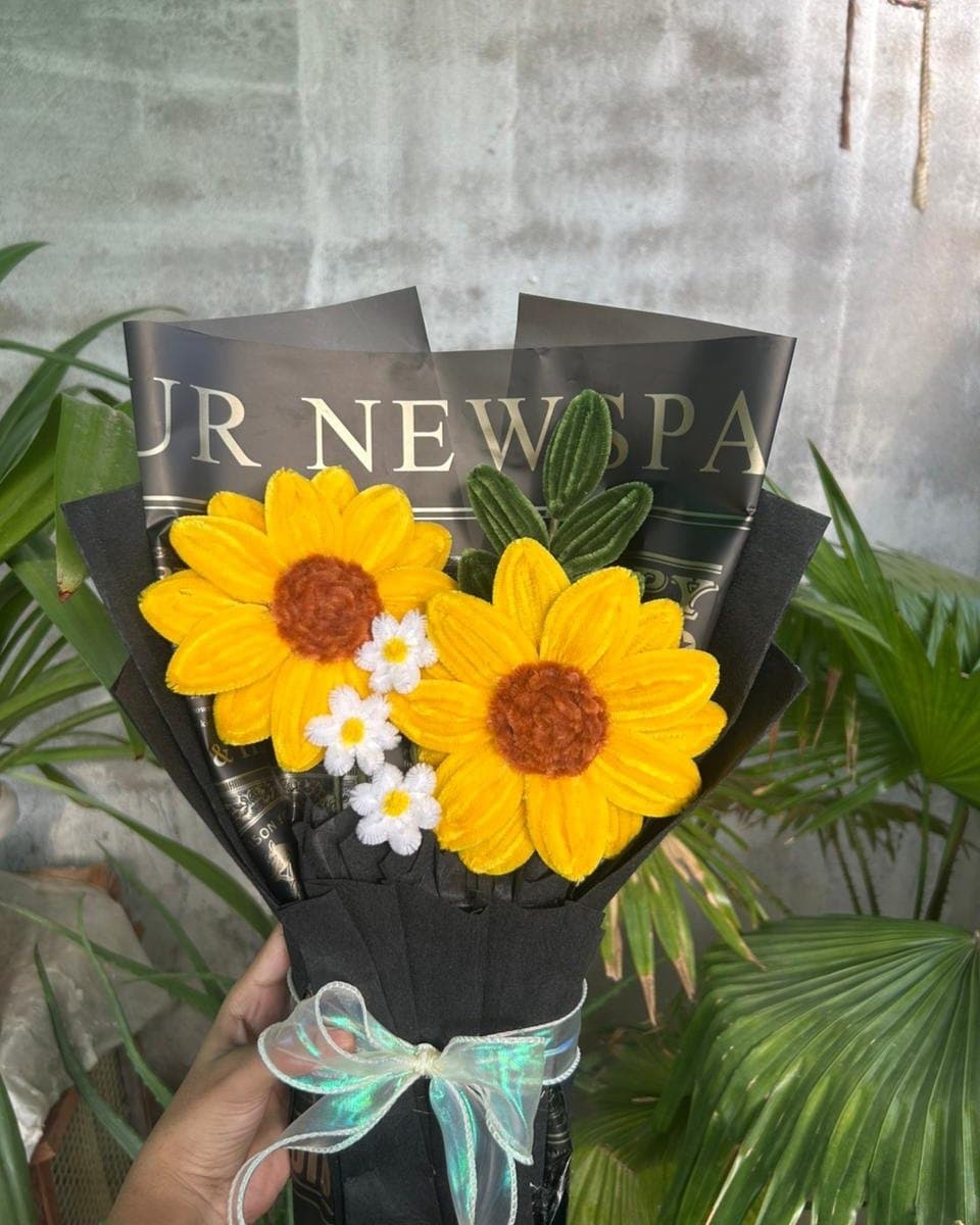 Pipe cleaner bouquet of two yellow sunflowers and three white daisies in black newspaper-print wrap